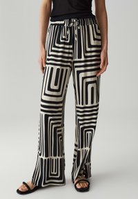Zwarte en crèmekleurige wijde broek met geometrische patronen, voorzien van een elastische tailleband en trekkoordafwerking. Gemaakt van een soepele stof.