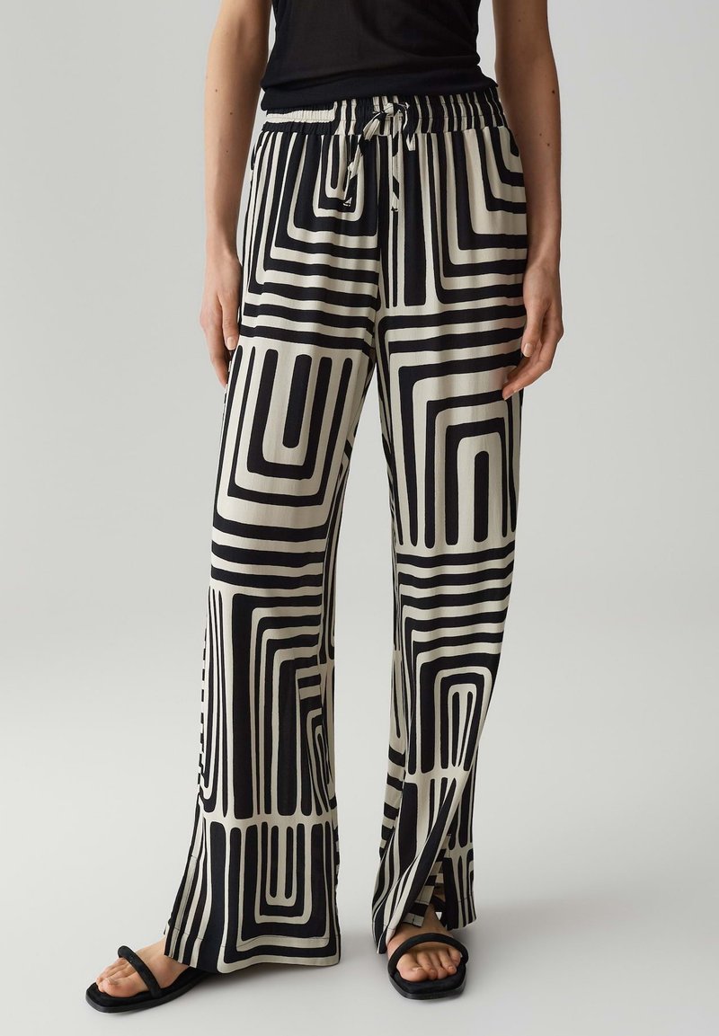 Zwarte en crèmekleurige wijde broek met geometrische patronen, voorzien van een elastische tailleband en trekkoordafwerking. Gemaakt van een soepele stof.