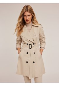 Palton bej cu un design cu două rânduri de nasturi, nasturi mari negri și o curea din același material. Dispune de mâneci lungi și buzunare laterale.