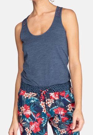 Canotta senza maniche di colore blu navy con dettagli in pizzo sulle spalle, abbinata a pantaloni a fantasia con un design floreale tropicale in colori vivaci.