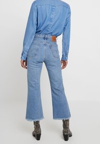 Light blue denim flared jeans with a frayed hem, high-rise waistband, and rear patch detailing, paired with a matching denim shirt.