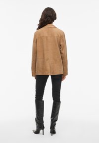 Brown suede jacket with a straight cut, single back seam, and notched collar, paired with black skinny jeans and knee-high boots.