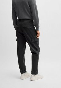 Ciemne spodnie cargo w paski, wykonane z teksturowanej tkaniny, z kieszeniami bocznymi i zwężającym się krojem, zestawione z białymi trampkami.