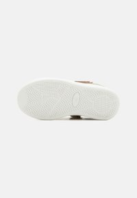 Talpa de sneaker cu o suprafață din cauciuc alb texturat, având modele zigzag și circulare pentru aderență și durabilitate.