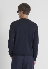 Marineblauwe trui met lange mouwen, ronde hals, geribbelde onderkant en schouderdetails. Zachte textuur, minimalistisch ontwerp, geschikt voor casual kleding.