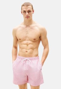 Shorts de bain rayés roses avec une taille élastique et un cordon de serrage. Possède des poches latérales et un petit logo sur la jambe.