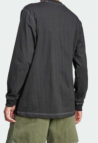 Svart långärmad skjorta med vita vertikala nålrandiga ränder, utrustad med rundad halsringning och kontrasterande manschetter, kombinerad med gröna cargoshorts.