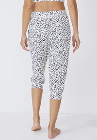 Pantaloni capri bianchi con una stampa leopardata nera, caratterizzati da un design aderente e da polsini elasticizzati alla caviglia, che mostrano una texture di tessuto liscia.