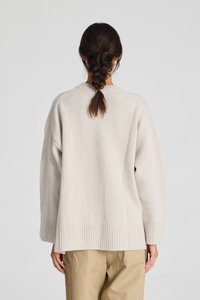 Lichtbeige oversized gebreide trui met ribgebreide zoom en manchetten. Relaxte pasvorm, zachte textuur en ronde halslijn, gedragen met tan kleurige broek.