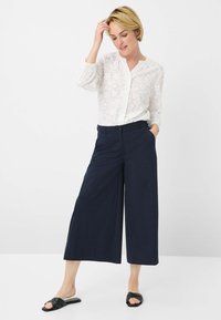 White, embroidered blouse with a V-neck and gathered sleeves paired with dark navy, wide-leg trousers and black slide sandals.