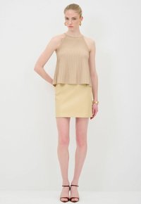 Beige geribbelde mouwloze top met een losse pasvorm, gecombineerd met een aansluitende lichtgele minirok. Model draagt bruine sandalen met bandjes.