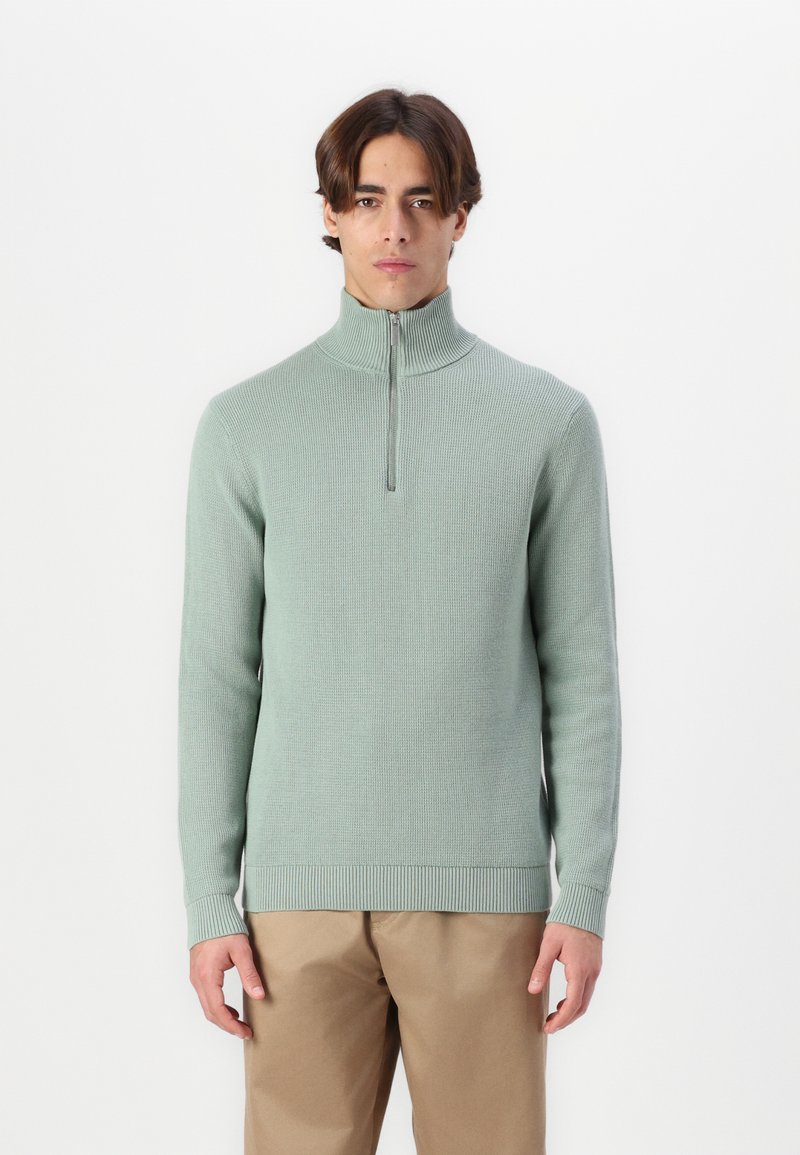 Light green knitted sweater with a high collar and half-zip closure, featuring ribbed cuffs and hem for a snug fit.