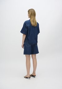 Completo in denim con una maglietta a maniche corte e aderente e pantaloni corti al ginocchio, entrambi di colore blu scuro. Presenta cuciture e tasche. Sandali neri con tacco.