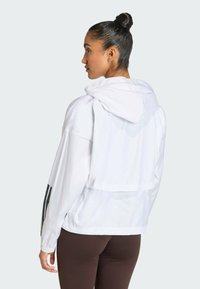 White windbreaker with a hood, featuring a loose fit, elastic cuffs, and black stripes on sleeves, made from lightweight, smooth material.