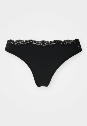 Zwarte stringonderbroek van gladde stof, met een gegolfde kantafwerking op de tailleband en een klein logologo aan de zijkant.