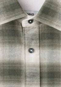 Camisa a cuadros verde y beige con un cuello clásico, un botón oscuro y una tela suave y texturizada. La etiqueta dice "MNG."
