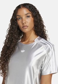 Maglietta atletica in satin argento caratterizzata da un design leggero, maniche corte e tre strisce bianche su ciascun spalla, con un piccolo logo sul petto.