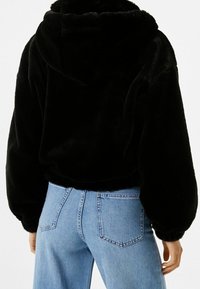 Svart faux fur hoodie med en kortad design, elastisk midja och huva. Matchad med ljusblå jeans med hög midja.