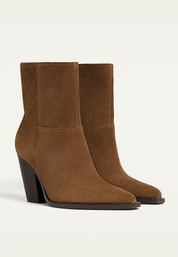 Bottines en daim marron avec bouts pointus et talons blocs empilés, présentées côte à côte sur un fond blanc.