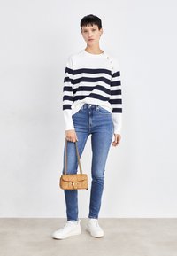 Navy and white striped sweater with buttons on one shoulder, paired with blue skinny jeans, white sneakers, and a tan quilted handbag.