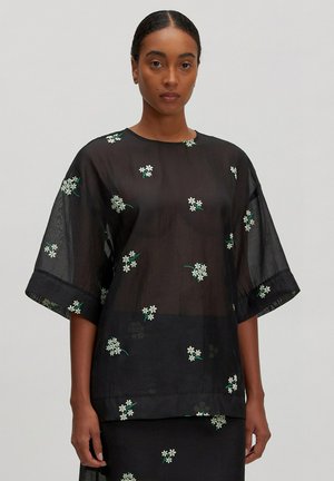 Schwarze durchsichtige Bluse mit kurzen, weiten Ärmeln, die mit weißen Blumenstickereien und grünen Stielen verziert ist. Glatte Textur, lässiges Design, leichtes Material.
