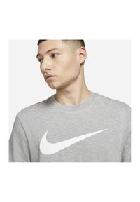 Grå bomulds T-shirt med rund hals, prydet med et fremtrædende hvidt Nike swoosh-logo på forsiden. Minimalistisk design, korte ærmer.