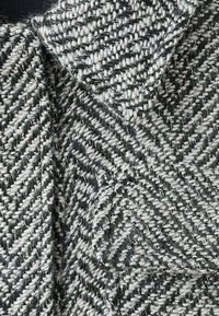 Wool-blend fabric in a herringbone pattern, featuring gray and white threads, with a textured finish and pointed collar detail.