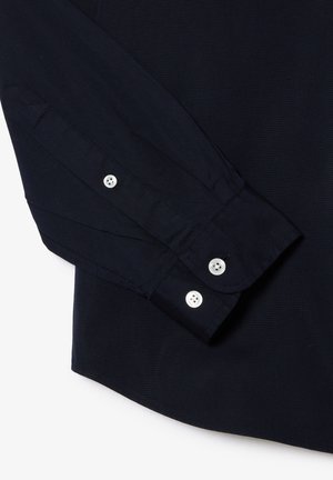 Camicia a maniche lunghe blu navy con polsini abbottonati, realizzata in tessuto morbido, caratterizzata da cuciture distintive e orlo arrotondato. Bottoni argentati completano il design.