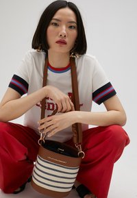 Brown and white striped bucket bag with a braided shoulder strap, metal hardware, and a dark interior, displayed in a casual outfit.