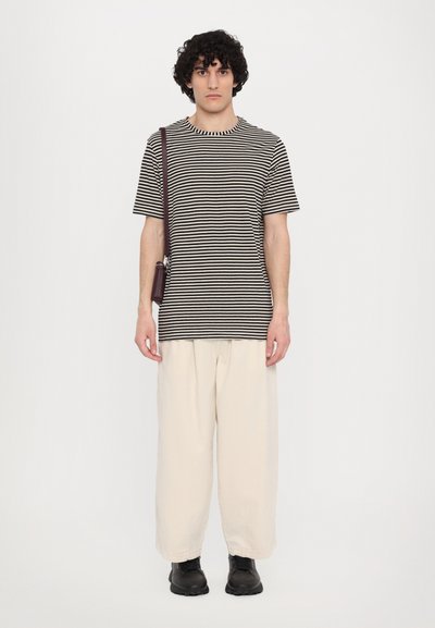 Tricou cu dungi în alb și negru, din bumbac, cu guler rotund; asortat cu pantaloni cremoși, lejeri și încălțăminte neagră. Geantă de umăr casual.