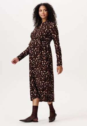 Femme enceinte aux cheveux bouclés portant une robe midi à manches longues imprimée léopard, des chaussettes marron et des ballerines pointues, marchant légèrement.