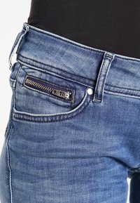 Tmavě modré džíny z denimu se slim fit, předními kapsami a malou zapínací kapsičkou na pravé straně blízko pasu.