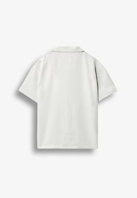 Chemise blanche à manches courtes vue de dos avec un ourlet droit et un col plat sur un fond clair uni.