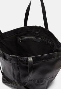 Czarna skórzana torba tote z dwiema długimi rączkami, wewnętrzną kieszenią na zamek, gładką teksturą i wytłoczonym logo marki z boku.