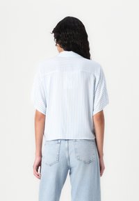 Light blue and white striped short-sleeve shirt with a loose fit, featuring a back yoke and relaxed silhouette, paired with light denim jeans.