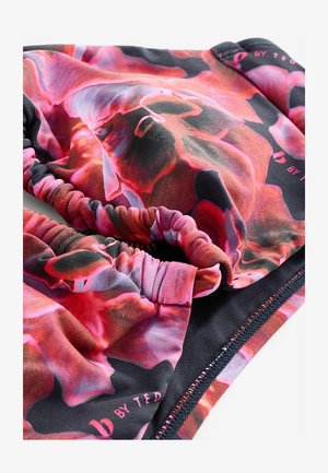 Barvno blago s cvetnim vzorcem, ki vključuje roza, rdeče in črne odtenke. Zbrani elastični robovi in gladka tekstura, označeno z "by TED."