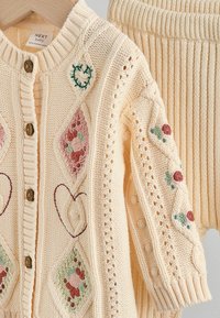 Strik cardigan i blød crepe med træknapper, der har blomsterbroderi og blondedetaljer på ærmerne. Ribbede krave og kant.