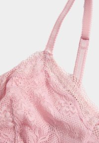 Pink lace bralette featuring floral patterns, adjustable straps, and a delicate scalloped edge along the neckline and straps.