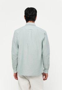 Lys grøn skjorte med knapper, slim fit, myk tekstur og bakstykke. Har lange ermer og knappelukking ved ermer.