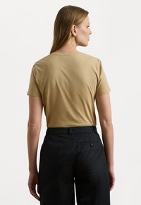 Kaki T-skjorte med korte ermer og rund hals, glatt tekstur og avslappet passform, kombinert med svarte bukser med baklommepreg.