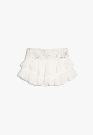 Mini-jupe blanche à volants superposés avec une ceinture en dentelle à œillets.