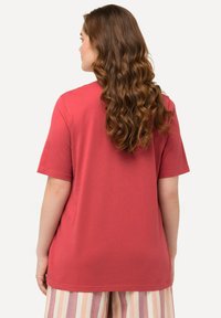 Červené bavlněné tričko s krátkým rukávem, volný střih, kulatý výstřih, hladká textura a rovný lem. Nosené s pruhovanými kalhotami.