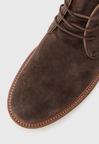 Brown suede leather dress shoe with round toe, stitched welt, and lace-up closure on white background.