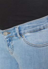 Os jeans de denim azul claro apresentam um fecho padrão com botão e zíper, com costuras laranja em contraste e um bolso frontal.