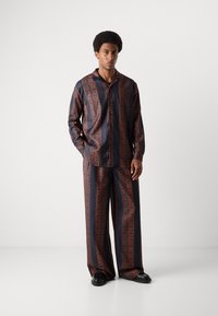 Conjunto de azul oscuro con estampado, compuesto por una camisa de botones de corte holgado y pantalones de pierna ancha, que presentan intrincados diseños geométricos naranjas y un tejido liviano.