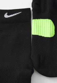 Zwarte sport sokken met een textuurweefsel, voorzien van een reflecterend zilveren logo en een felgroene geribbelde accent aan de zijkant.