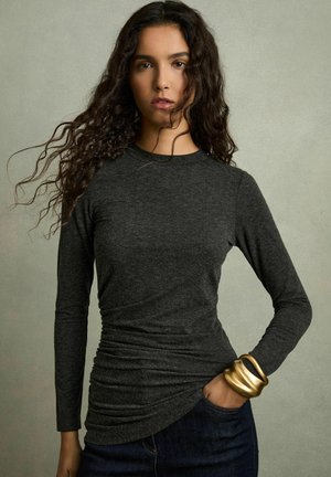 Hallide hall sleeves ja ümar kaelus, pehmed kogud detailiga vööl. Kombineeritud tumedate teksadega, randmel kuldne käevõru.