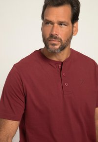 Bordový krátký rukáv pánský hladký triko ze 100% bavlny. Obsahuje tři knoflíky vpředu, kulatý výstřih a diskrétní výšivku loga na hrudi.