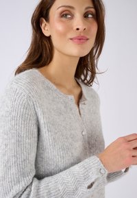 Graue Strickjacke mit rundem Ausschnitt, Knopfleiste und Fischgrätmuster an den Bündchen. Der Stoff hat ein weiches, flauschiges Aussehen.