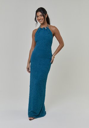 Vestido de cuello halter color azul verdoso con tela texturizada y con ondas. Silueta ajustada que cae hasta el suelo, con detalle de botones en el escote.